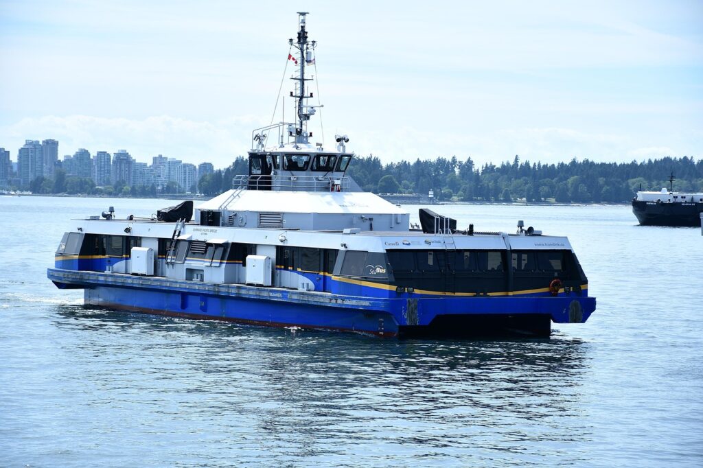 Fähre mit blau-weißem Rumpf fährt auf ruhigem Wasser, im Hintergrund Stadt und Bäume
